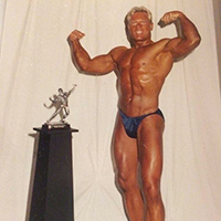 Advocate, Greg, posing with bodybuilding trophy after winning contest