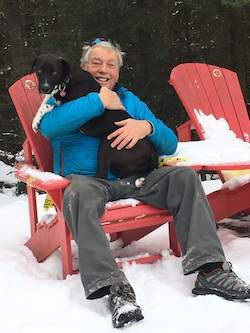 Cliff hugs a dog while sitting on a snowy deck chair