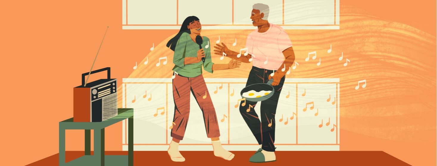 Senior man and adult woman singing along to music in the kitchen.